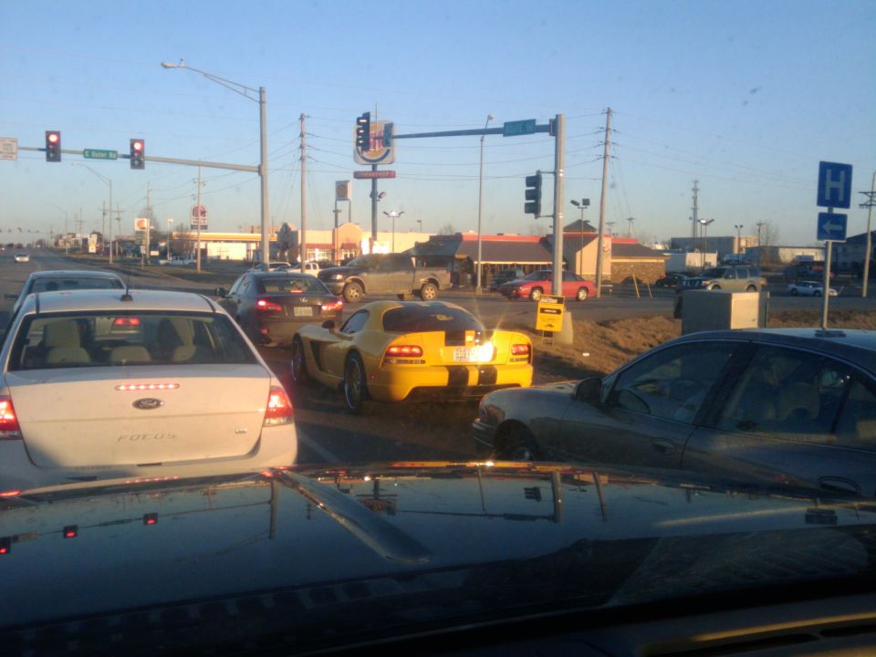 Yellow sports car with black racing stripes on the rear, stopped in traffic