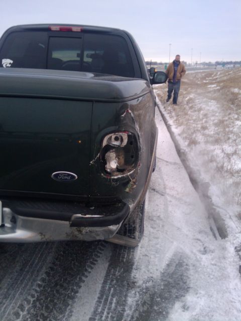 2005 Ford F-250 - A dark green Ford pickup truck is seen from the rear with a damaged taillight. A man walks away in the snowy background.