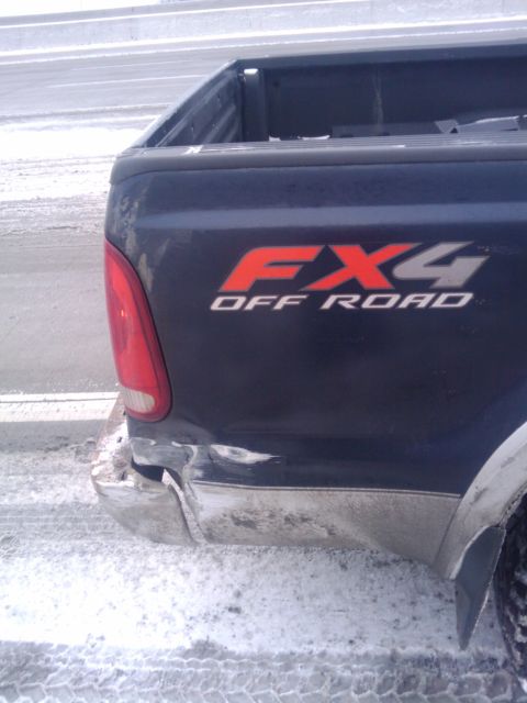 2005 Ford F-250 - Dark pickup truck with FX4 Off Road decal and damaged bumper, seen in winter conditions.
