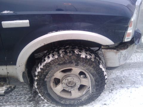 2005 Ford F-250 - Front wheel and fender of a dark blue 2005 Ford F-250, partially covered in snow.