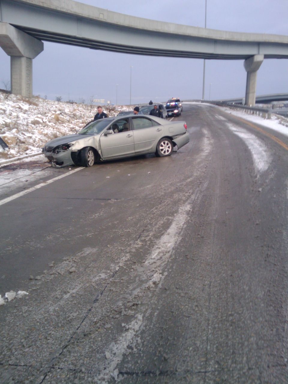 Silver sedan with front-end damage on a wet, snowy highway under an overpass