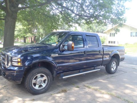 2005 Ford F-250 - This dark blue 2005 Ford F-250 crew cab pickup truck is seen from a three-quarter front angle, parked outdoors under a tree.