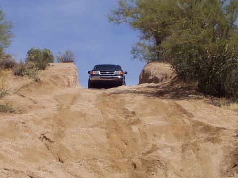 1993 Ford Bronco - A black SUV navigates a steep, sandy incline under a clear blue sky, with sparse desert vegetation surrounding the path.