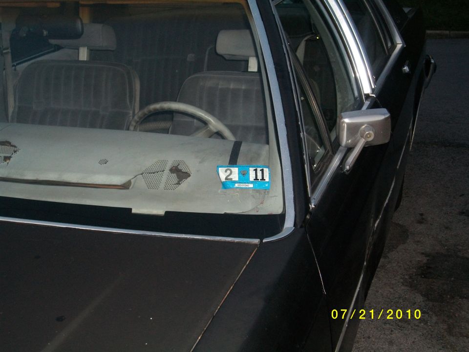 Car interior with cracked dashboard, gray seats, and a blue registration sticker on the windshield