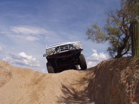 1993 Ford Bronco - White Ford Bronco navigating a steep dirt incline under a partly cloudy sky.