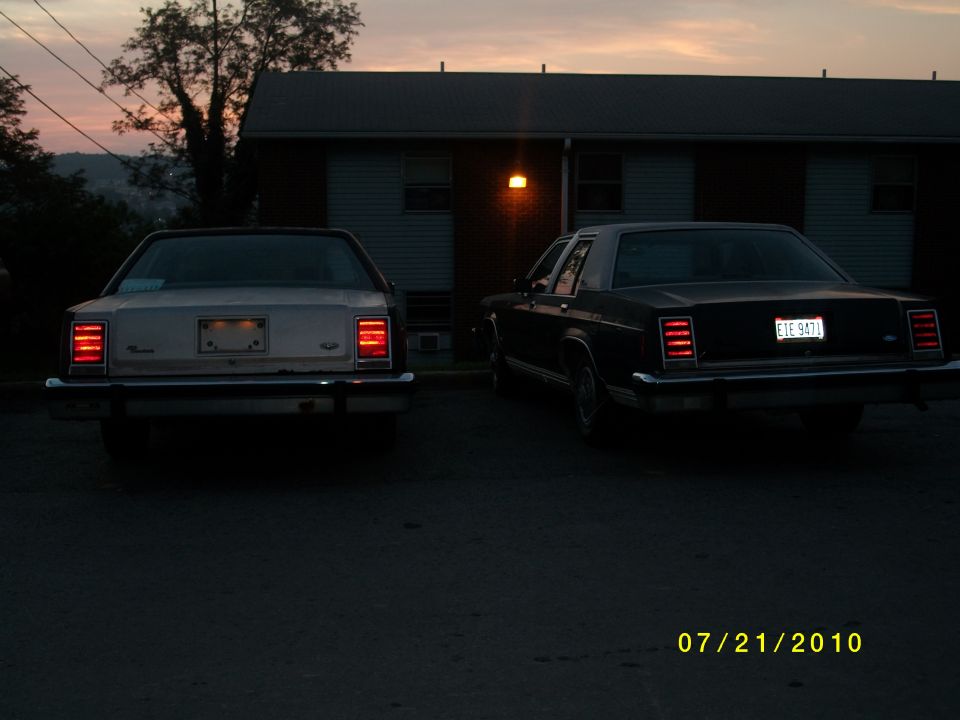 Two 1987 Ford Crown Victoria LTD sedans parked in a lot at dusk. The one on the right has license plate EIE 9871