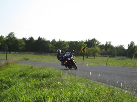 2008 Yamaha FZR1000 - A motorcycle navigates a curve on a road bordered by grass and trees under a bright sky.