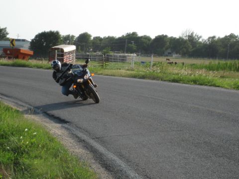 2008 Yamaha FZR1000 - Rider takes a corner on a motorcycle on a rural road with farm scenery.