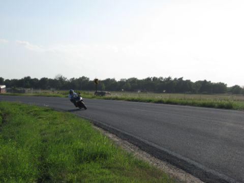 2008 Yamaha FZR1000 - A lone motorcycle navigates a curve on a paved road bordered by grassy fields and trees under a hazy sky.