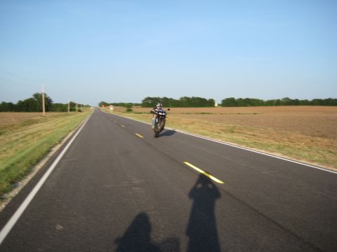 2008 Yamaha FZR1000 - Motorcycle performing a wheelie on a straight, empty road under a clear blue sky.