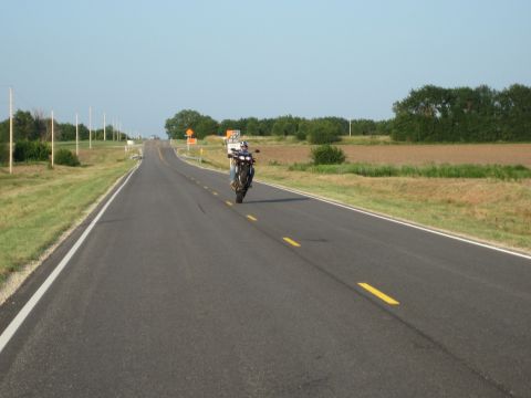 2008 Yamaha FZR1000 - Motorcycle performs a wheelie on an open highway with fields and trees in the background under a clear blue sky.