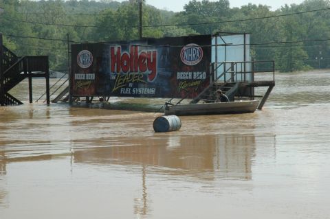2007 Ford Mustang - A flooded drag strip shows a boat navigating the water near a large Holley banner, with a barrel floating nearby.