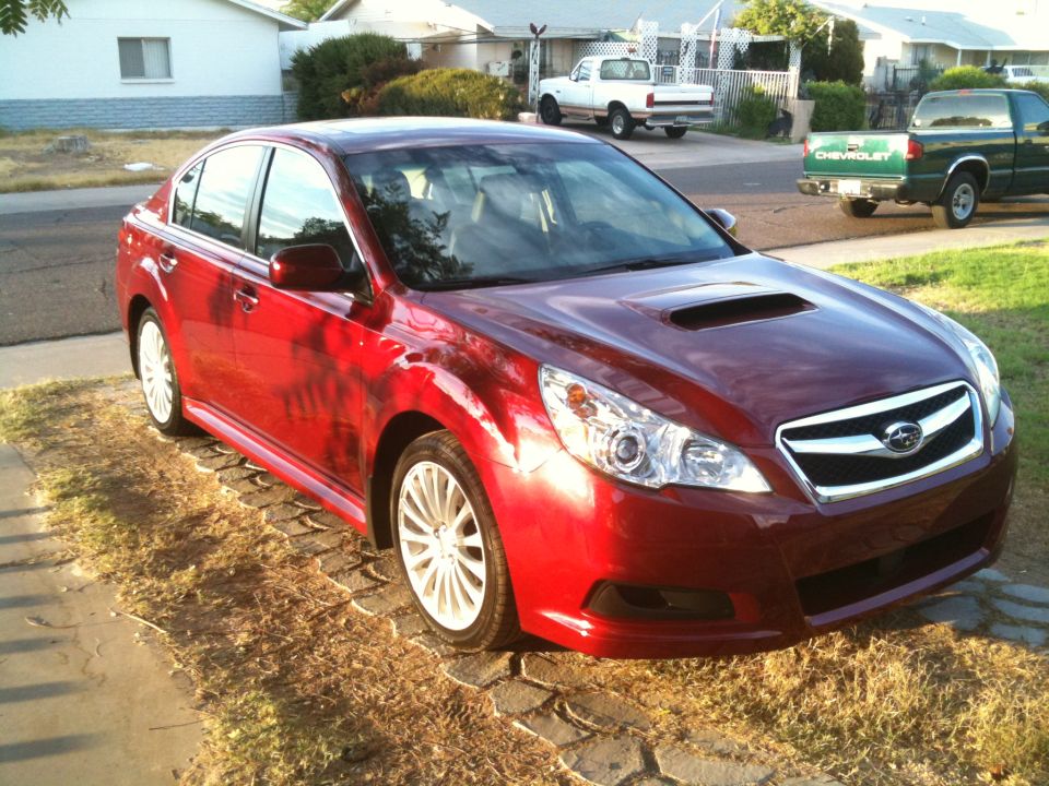 Red 2010 Subaru Legacy sedan parked on a cobblestone driveway, front 3/4 view