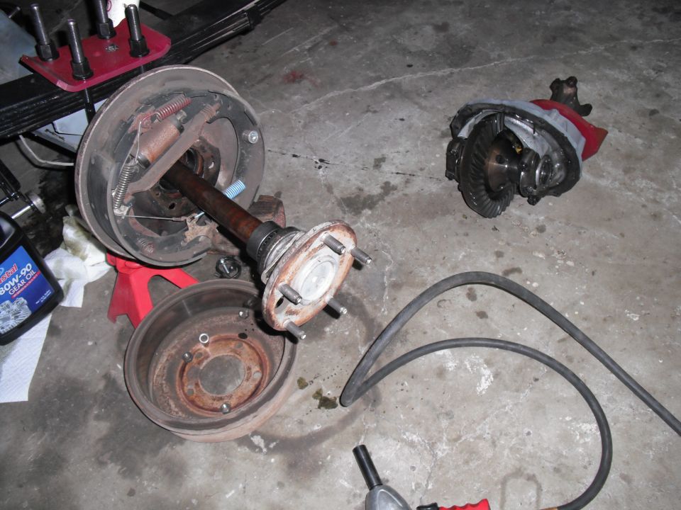 Vehicle axle, brake drum, and differential laid out on concrete floor. Bottle of gear oil nearby
