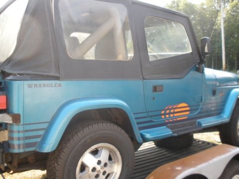 1991 Jeep YJ - A blue 1991 Jeep YJ Wrangler is viewed from the side, showing its soft top and distinctive side decal.