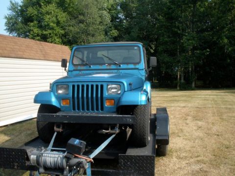 1991 Jeep YJ - This blue Jeep YJ is seen on a trailer, presenting its iconic front grille and headlights.
