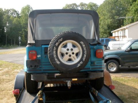 1991 Jeep YJ - This teal 1991 Jeep YJ is seen from the rear, with its spare tire prominently displayed on the tailgate.