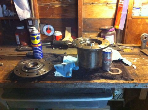 1989 Ford Bronco - Automotive parts, including a differential housing and flange, are laid out on a workbench next to a can of beer and lubricant.