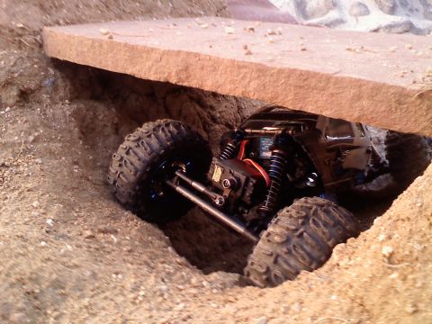 1996 Ford Bronco - A black remote control rock crawler is shown navigating a challenging dirt path beneath a large rock formation.