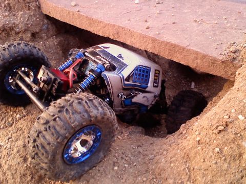 1996 Ford Bronco - RC rock crawler is stuck in a narrow dirt gap, its large tires unable to gain traction.