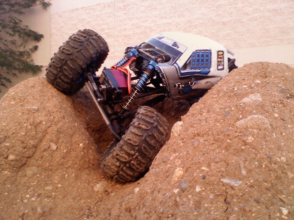 RC rock crawler vehicle climbing over dirt mounds, showing suspension and large tires