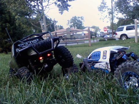 1996 Ford Bronco - Two RC rock crawlers sit in the grass, one with a prominent roll cage and spare tire.