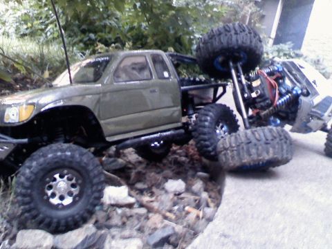 1996 Ford Bronco - Two remote-control trucks are positioned on a rocky terrain, with one appearing to be climbing over the other.