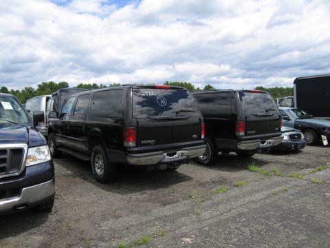 2001 Ford Crown Victoria - Two black Ford Excursions are parked side-by-side in an outdoor lot under a cloudy sky.