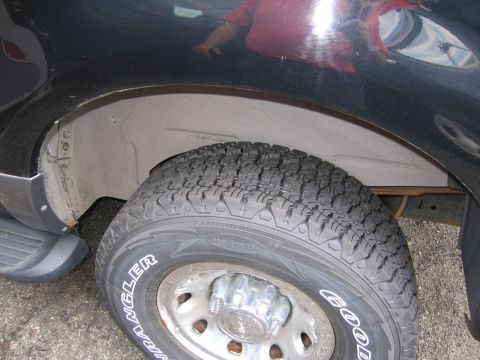 2001 Ford Crown Victoria - The rear wheel well and tire of a truck are shown, with "GOODYEAR WRANGLER" text on the tire.