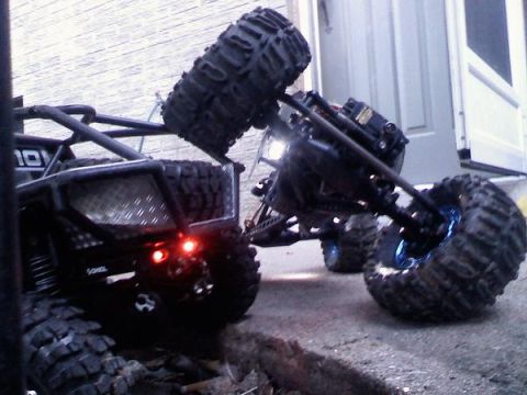 1996 Ford Bronco - Two remote control rock crawlers are shown on pavement, one tilted on its side.