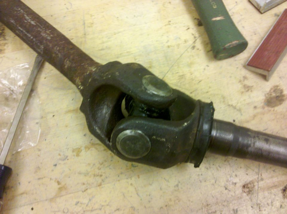 Rusty front axle shaft with U-joint and splined stub shaft on a plywood workbench