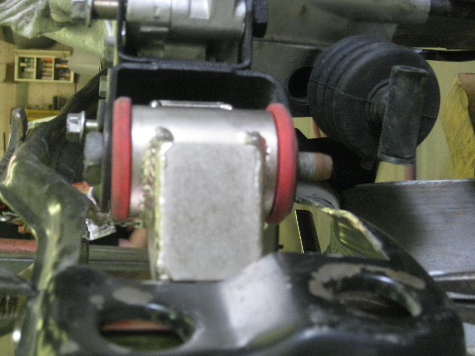 Close-up of a silver suspension component with red bushings, bolted to black metal