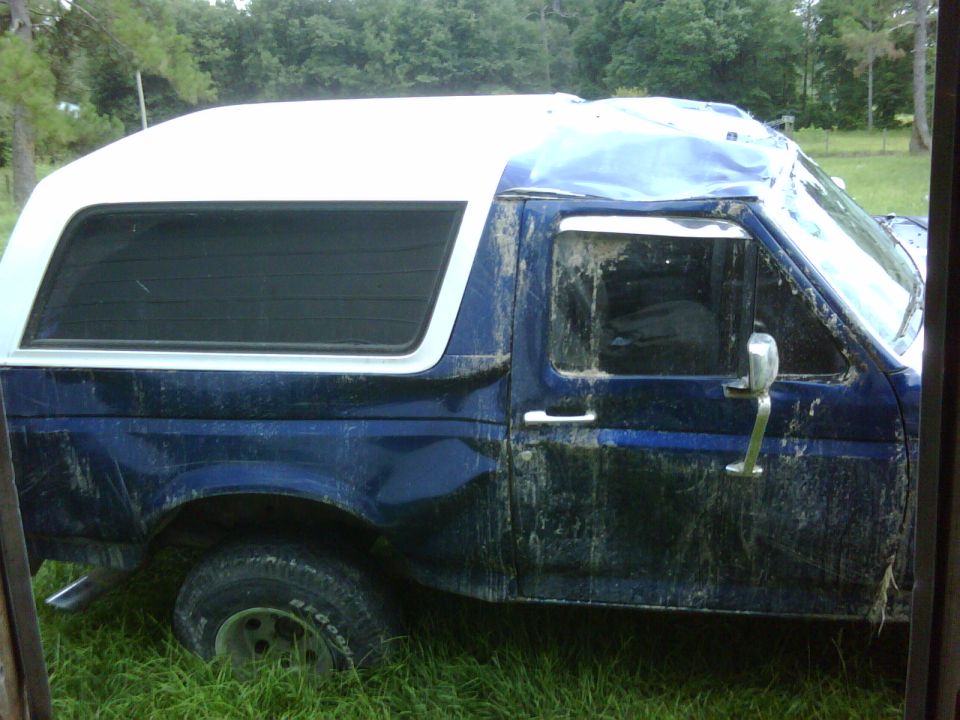 1991 Ford Bronco side view, blue body with white camper shell, covered in mud