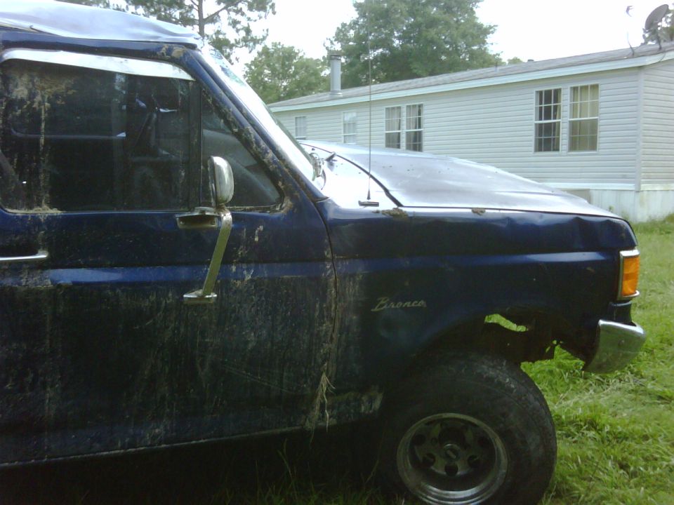 Blue Ford Bronco parked in front of a mobile home. The vehicle is covered in mud