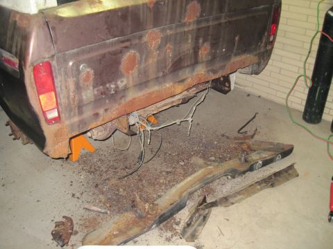 1979 Ford Bronco - This heavily rusted truck bed and frame are supported by jack stands, with various metal components scattered on the ground below.