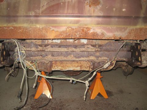 1979 Ford Bronco - The rear frame and wiring of a vehicle are heavily rusted and supported by orange jack stands.