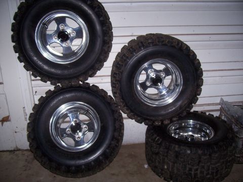 1978 Ford F-150 - A set of four off-road tires with shiny chrome rims are displayed against a white paneled wall.