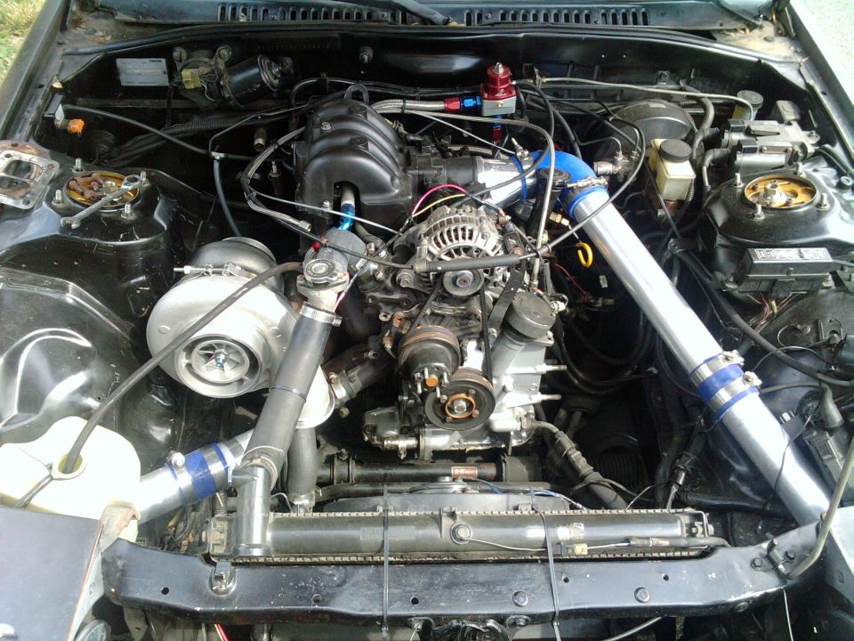 RX-7 engine bay with rotary engine, large single turbo, and polished intercooler piping with blue couplers