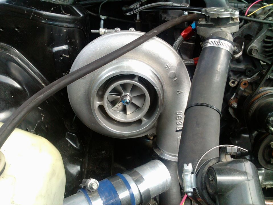 Close-up of a turbocharger mounted in an engine bay, with hoses and plumbing visible