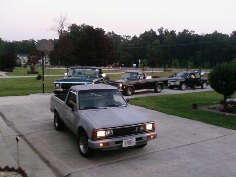 1979 Ford Bronco - A lineup of four pickup trucks is visible in a suburban driveway during the day.