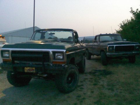 1979 Ford Bronco - Two Ford trucks, a green Bronco and a dark pickup, are parked outdoors under an overcast sky.