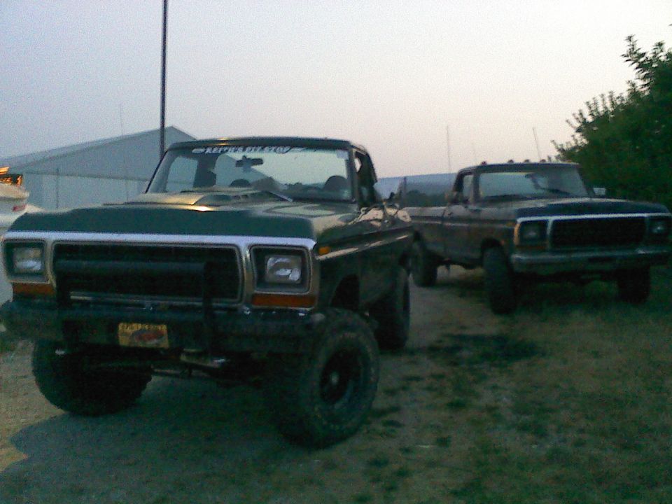 Green 1979 Ford Bronco with a hood scoop and a lifted suspension, parked next to a dark-colored Ford pickup truck