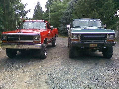 1979 Ford Bronco - Two lifted pickup trucks, a green 1979 Ford F-Series and a red Dodge, are parked on a gravel road.