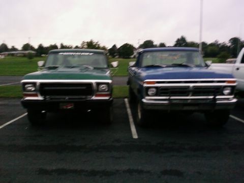 1979 Ford Bronco - Two vintage pickup trucks are parked in a lot under an overcast sky.