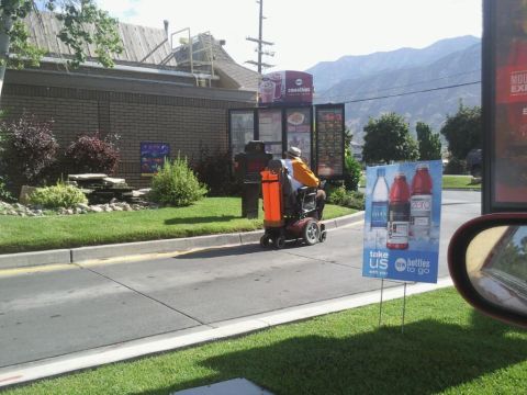 1991 Ford Bronco - A person on a mobility scooter navigates a drive-thru lane with a menu board and mountains visible.