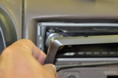 1996 Ford Bronco - Close-up of a hand removing a trim piece from a vehicle's dashboard, revealing the car stereo.
