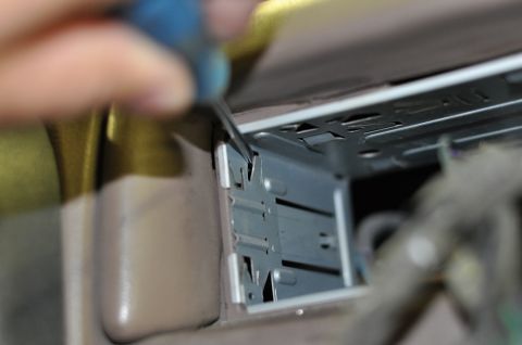 1996 Ford Bronco - Close-up of a hand working on a metal bracket within a car's interior.
