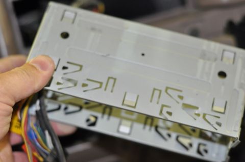 1996 Ford Bronco - A hand holds a metal car stereo mounting bracket with a bundle of colorful wires attached.
