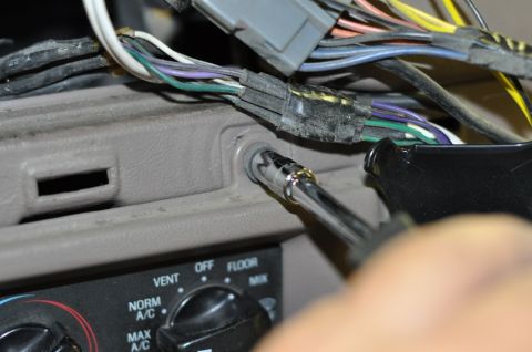 1996 Ford Bronco - A close-up view of a hand using a socket wrench on a screw within a vehicle's interior, surrounded by electrical wiring.