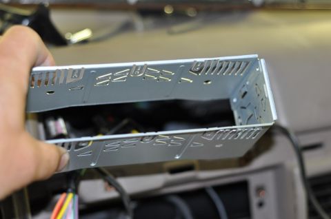 1996 Ford Bronco - A person is holding a metal mounting bracket for a car stereo, with wiring visible in the background.
